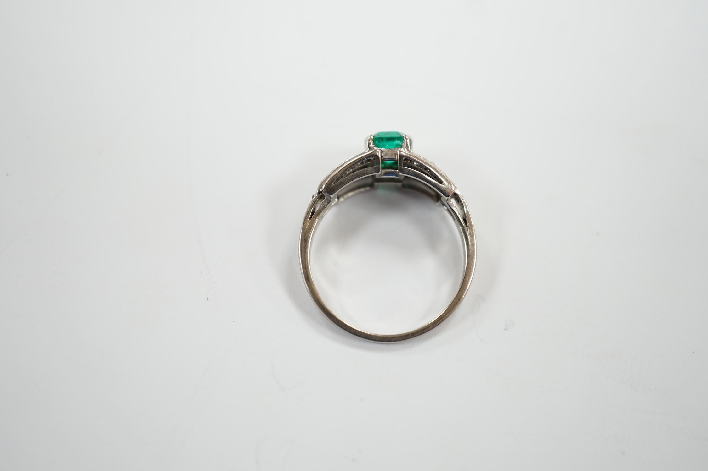 A white metal and octagonal cut emerald set dress ring, with diamond cluster set shoulders, size O, gross weight 3.6 grams.